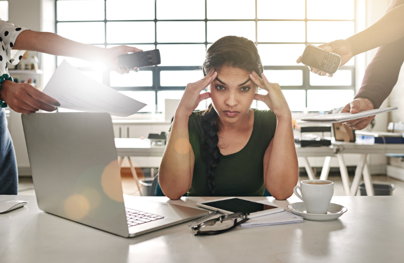 Woman with laptop looking overwhelmed by 3 people trying to hand her information