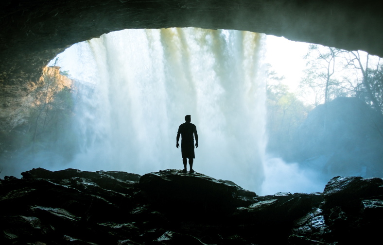 Person standing in a cave behind a waterfall